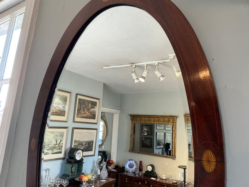 An antique oval mahogany wall mirror featuring a polished wooden frame accented with stringing inlay and four decorative marquetry medallions surrounding a bevelled mirror plate. View V