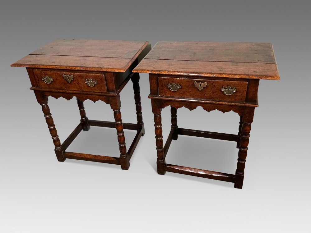 A matching pair of dark brown oak side tables featuring single frieze drawers with brass handles, turned legs, and square perimeter stretchers.