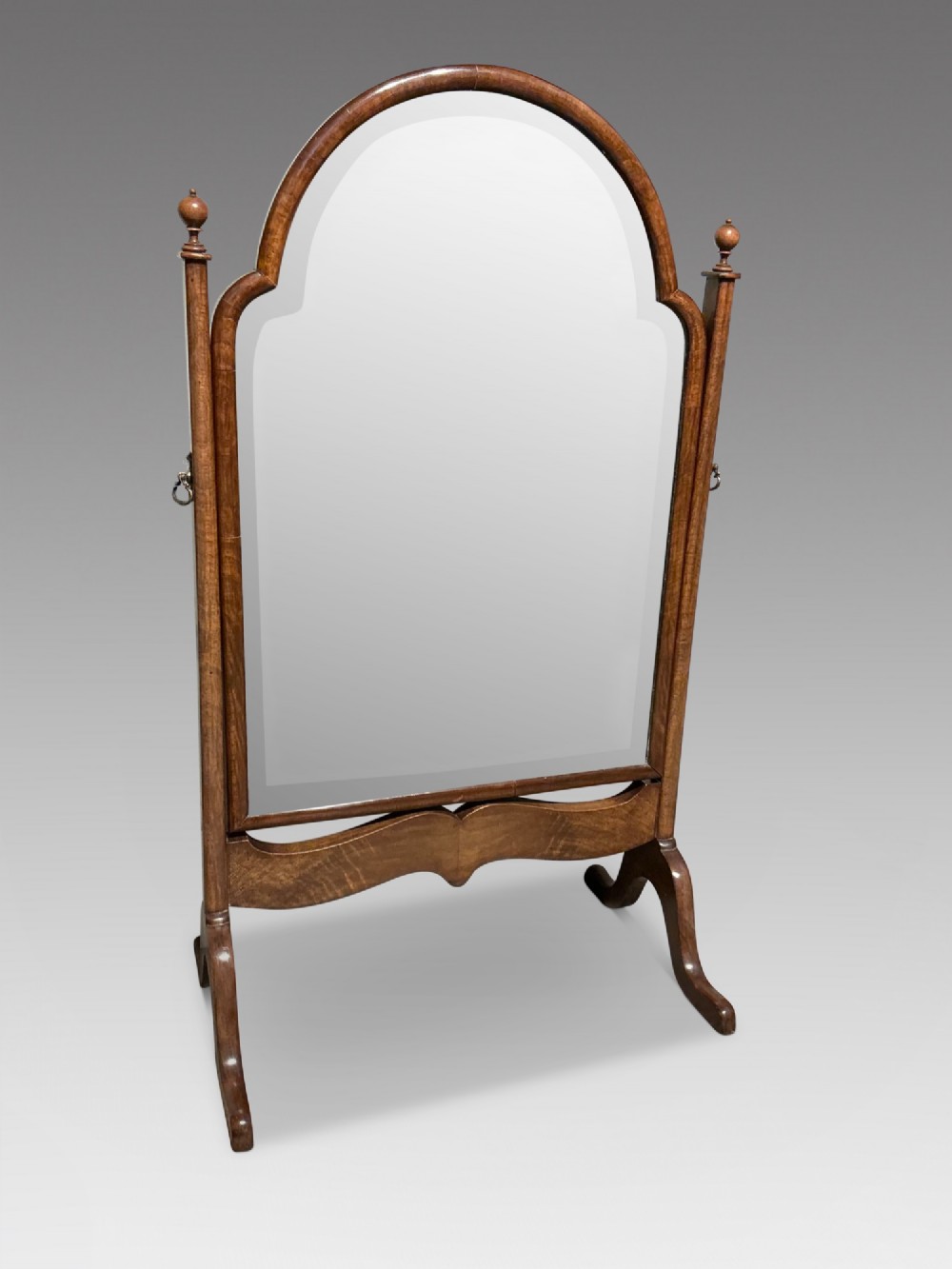 An antique arched walnut table mirror resting on vertical upright supports with turned finials and scrolled feet.