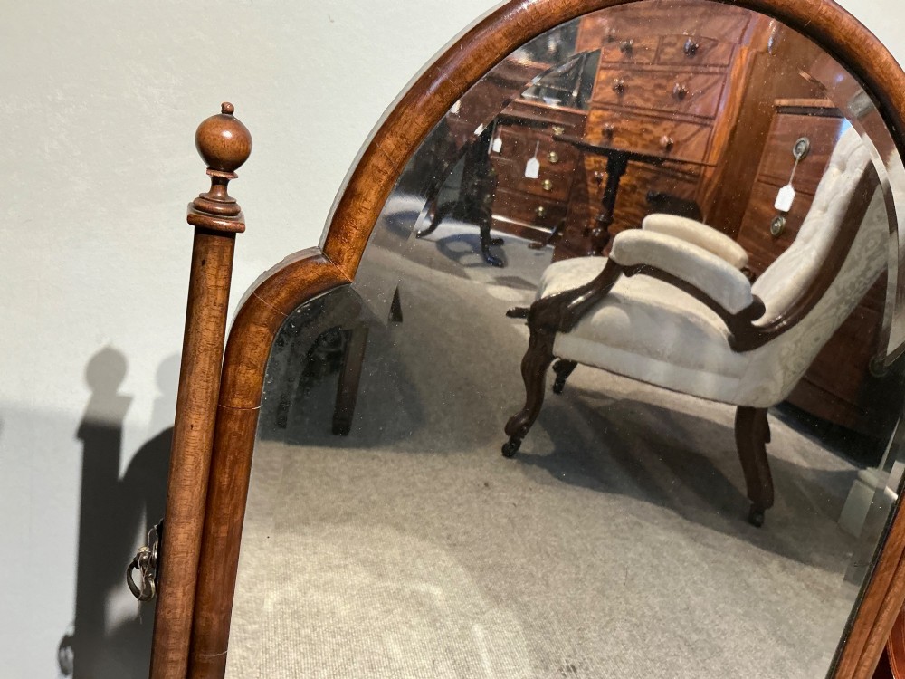 An antique arched walnut table mirror resting on vertical upright supports with turned finials and scrolled feet. View II