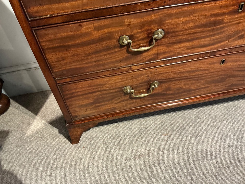 A Georgian mahogany chest of drawers featuring two short over three long graduated drawers with brass swan-neck handles and bracket feet. View V
