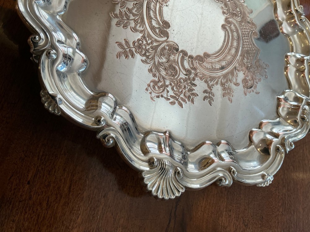 A circular silver-plated salver tray featuring an engraved scroll central pattern and a scalloped rim decorated with shell motifs. View II