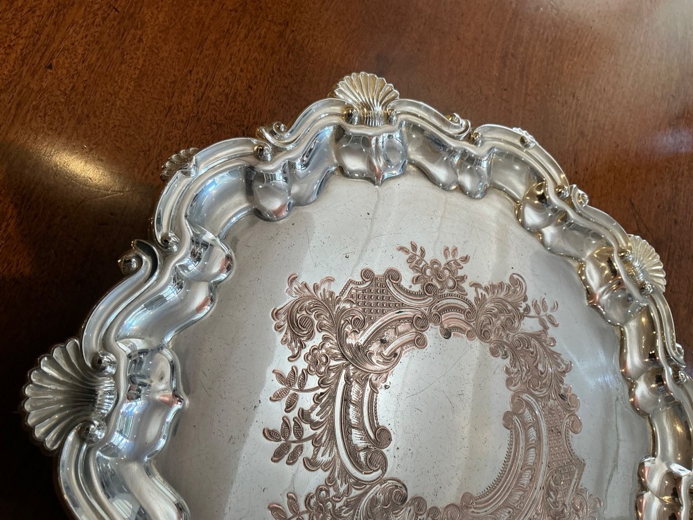 A circular silver-plated salver tray featuring an engraved scroll central pattern and a scalloped rim decorated with shell motifs. View III