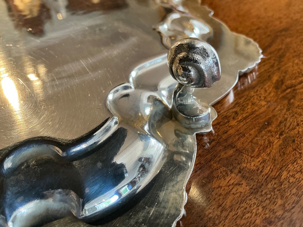 A circular silver-plated salver tray featuring an engraved scroll central pattern and a scalloped rim decorated with shell motifs. View V