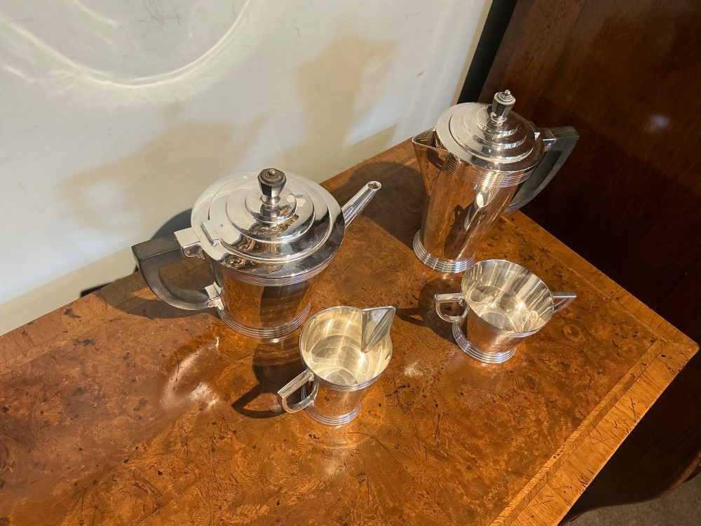 A four-piece Art Deco silver-plated tea and coffee service with angular handles and stepped lids set on a polished timber surface. View II