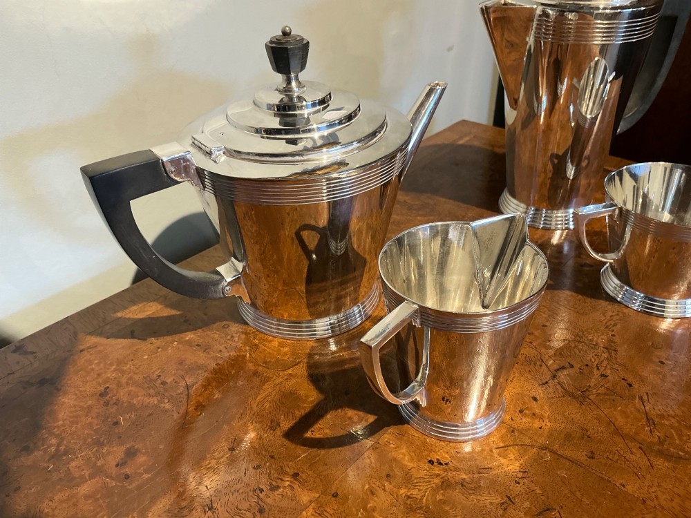 A four-piece Art Deco silver-plated tea and coffee service with angular handles and stepped lids set on a polished timber surface. View III