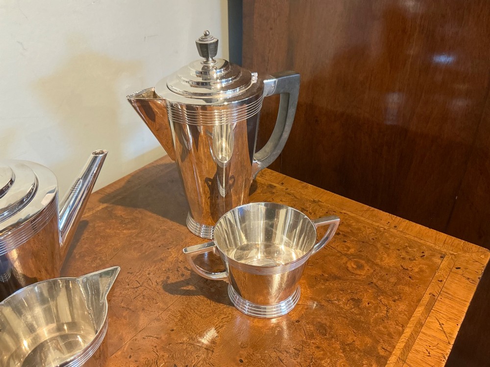 A four-piece Art Deco silver-plated tea and coffee service with angular handles and stepped lids set on a polished timber surface. View IV