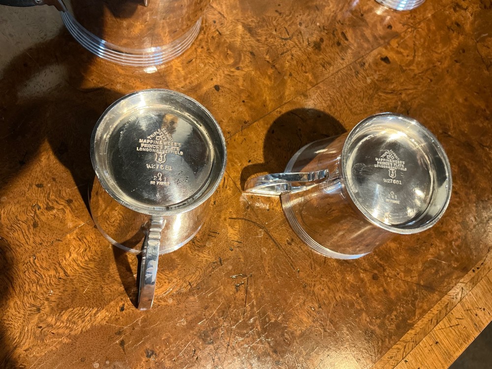 A four-piece Art Deco silver-plated tea and coffee service with angular handles and stepped lids set on a polished timber surface. View V