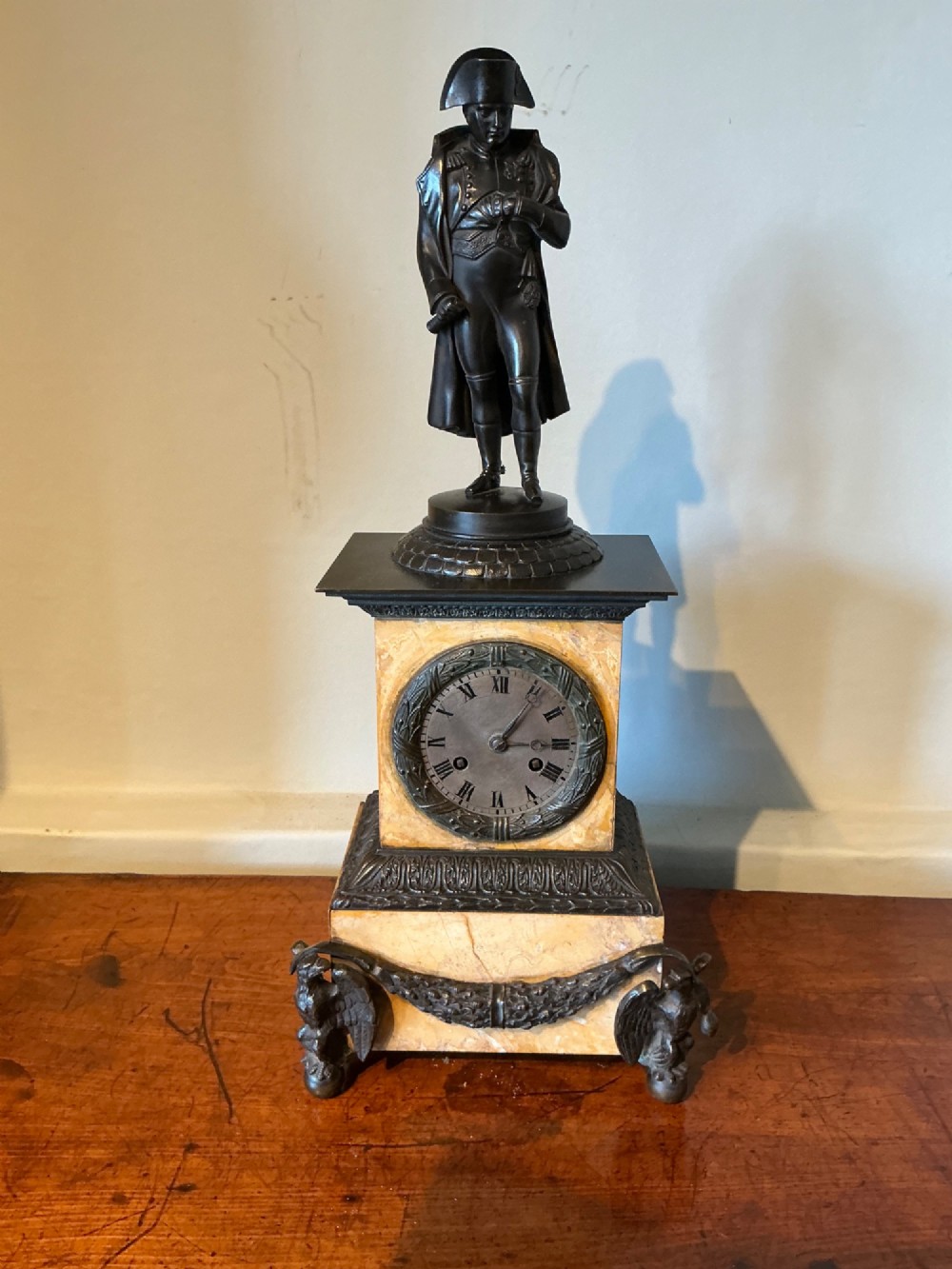 A French Empire style mantel clock featuring a dark patinated bronze figure of Napoleon standing above a yellow marble plinth housing a circular metal dial. View II