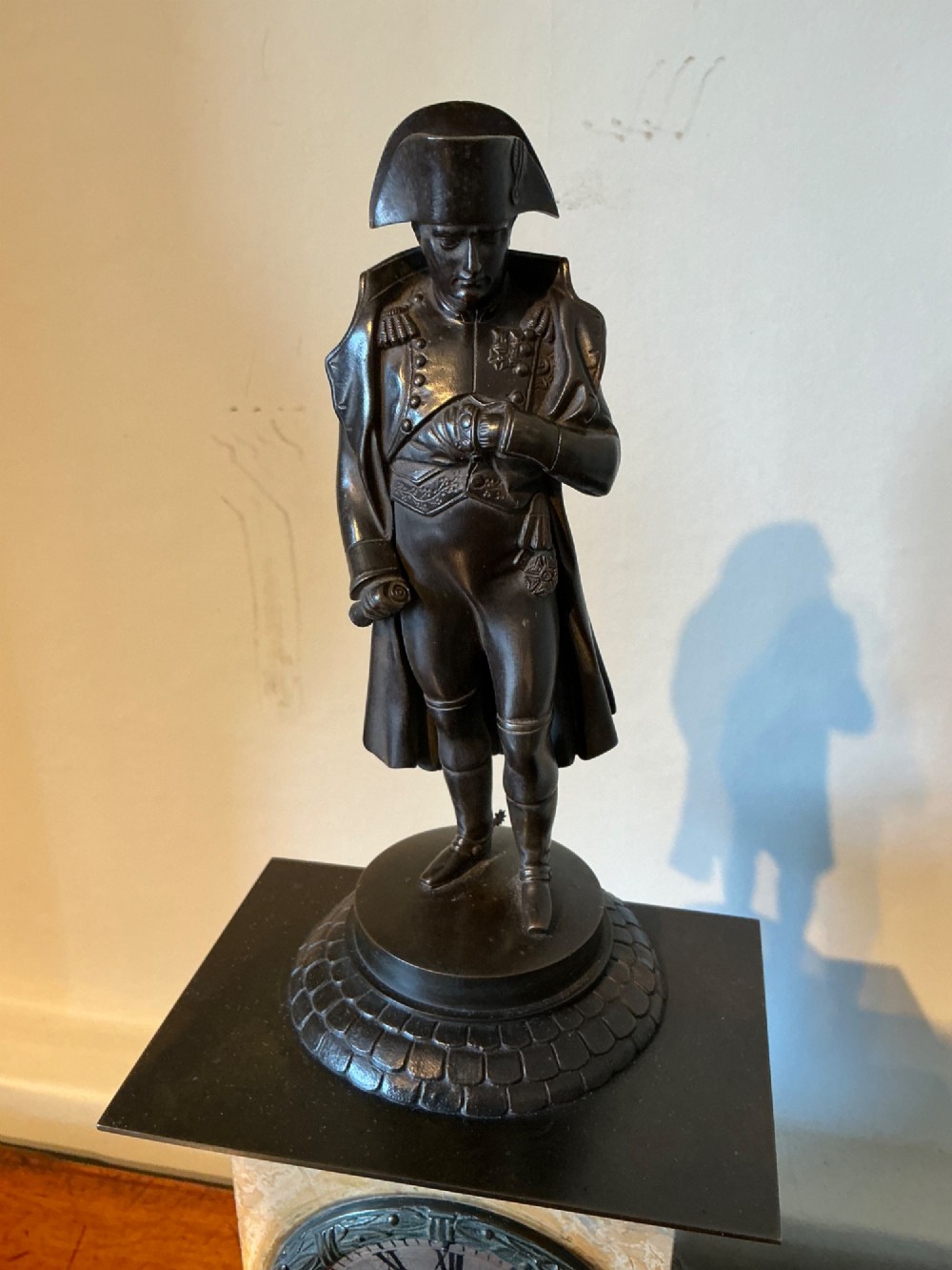 A French Empire style mantel clock featuring a dark patinated bronze figure of Napoleon standing above a yellow marble plinth housing a circular metal dial. View III