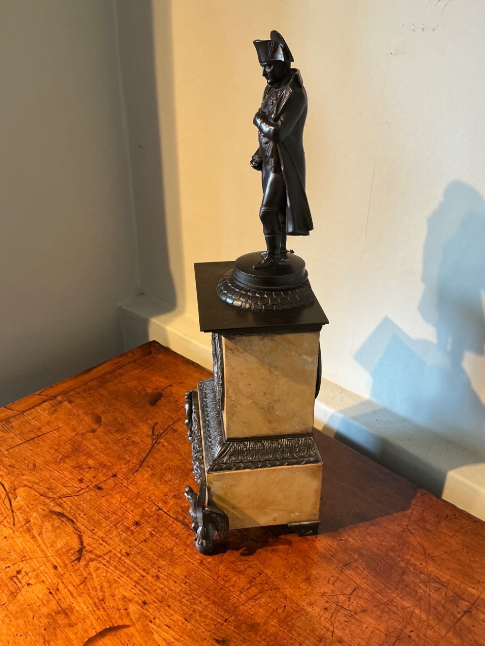 A French Empire style mantel clock featuring a dark patinated bronze figure of Napoleon standing above a yellow marble plinth housing a circular metal dial. View V