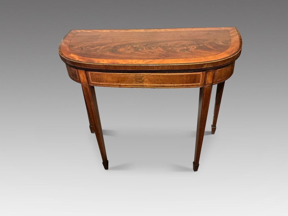 A D-shaped Georgian mahogany fold-over card table featuring flame mahogany veneers, contrasting inlay stringing, and tapered square legs.
