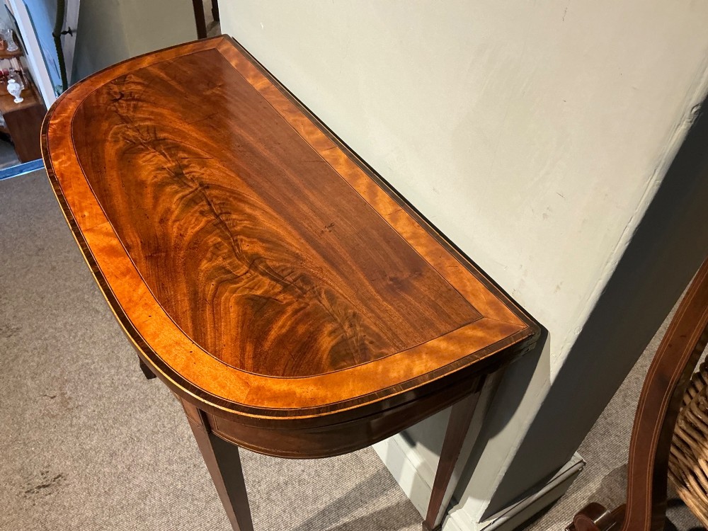 A D-shaped Georgian mahogany fold-over card table featuring flame mahogany veneers, contrasting inlay stringing, and tapered square legs. View IV