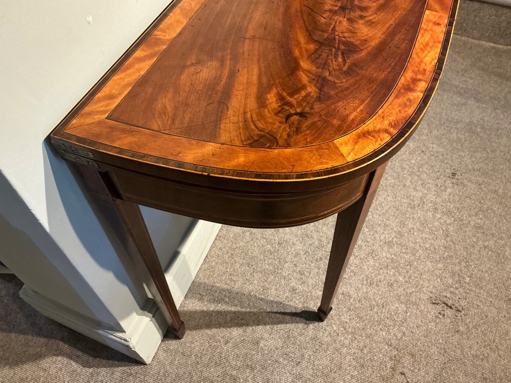 A D-shaped Georgian mahogany fold-over card table featuring flame mahogany veneers, contrasting inlay stringing, and tapered square legs. View V
