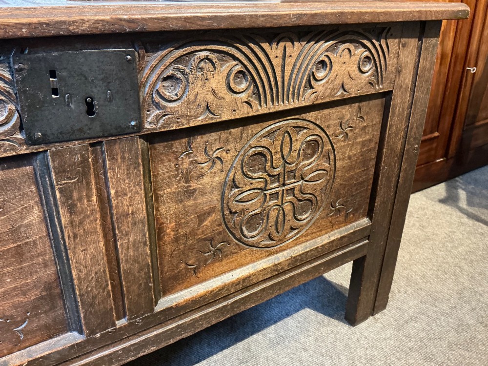 A 17th-century carved oak coffer with a four-panel lid, carved lunette top rail, roundel carved front panels, and a central iron lockplate. View V
