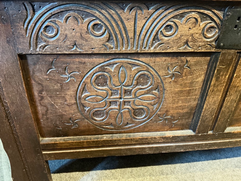 A 17th-century carved oak coffer with a four-panel lid, carved lunette top rail, roundel carved front panels, and a central iron lockplate. View VI