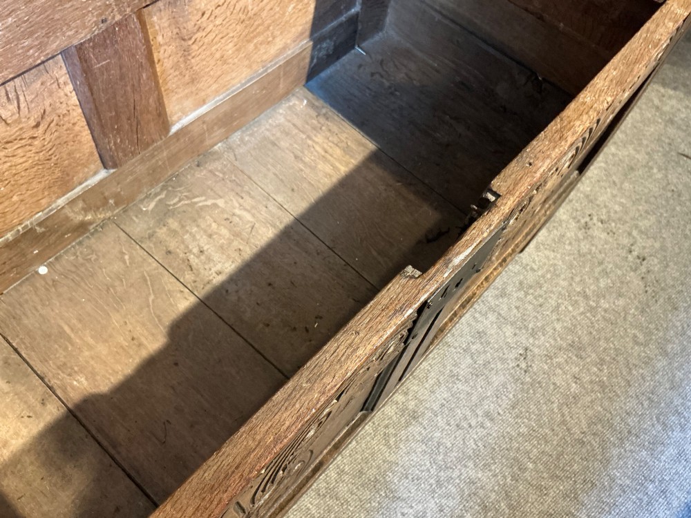 A 17th-century carved oak coffer with a four-panel lid, carved lunette top rail, roundel carved front panels, and a central iron lockplate. View X