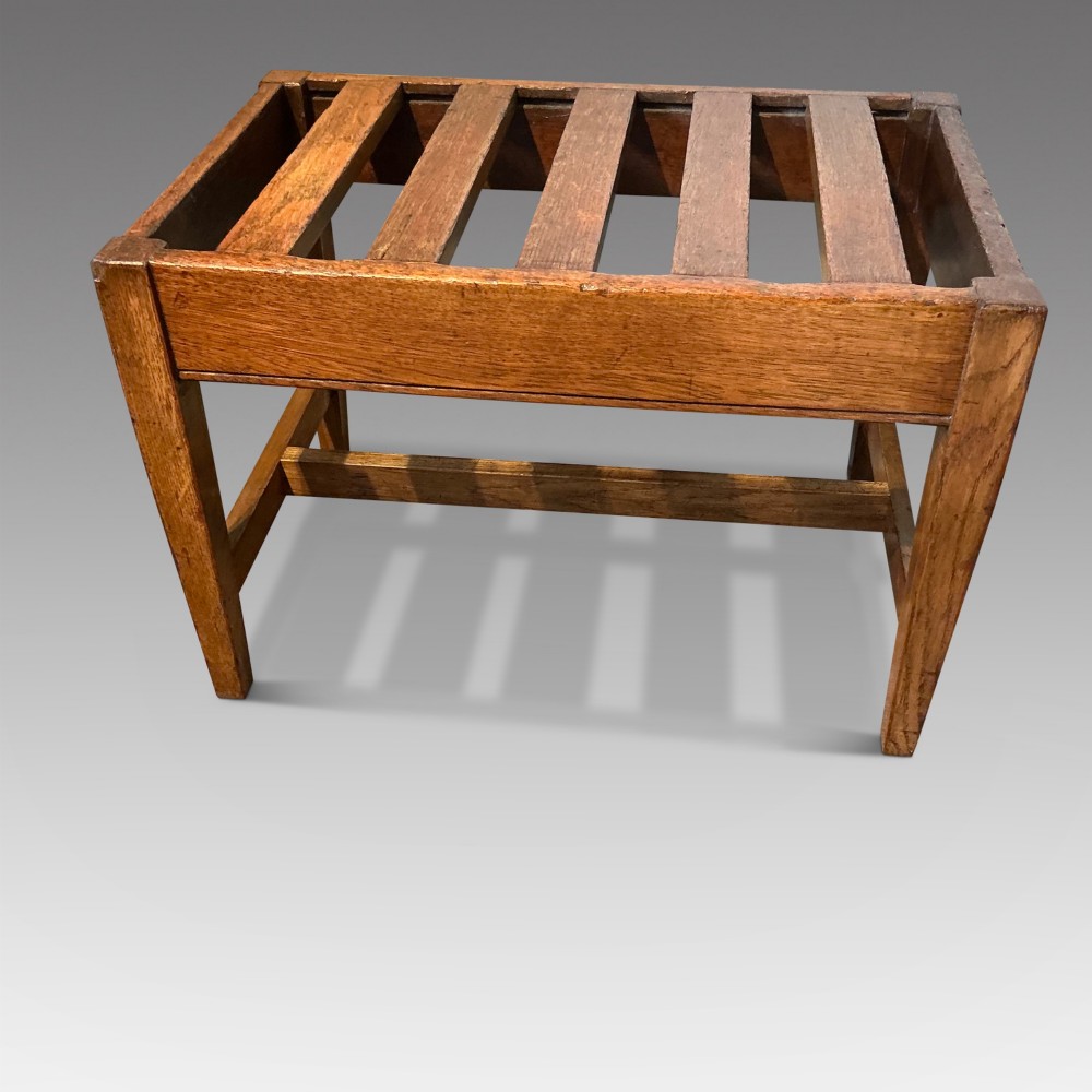 A solid oak antique luggage rack featuring five rectangular top slats supported by square legs and cross stretchers.