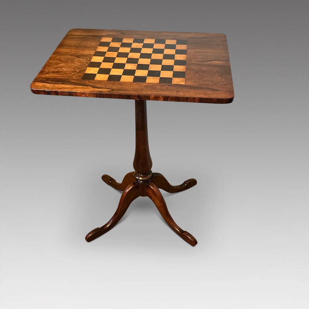 An antique dark wood pedestal chess table featuring an inlaid checkerboard surface top and a turned stem on four splayed legs.