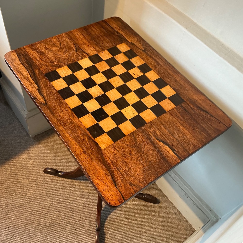 An antique dark wood pedestal chess table featuring an inlaid checkerboard surface top and a turned stem on four splayed legs. View III