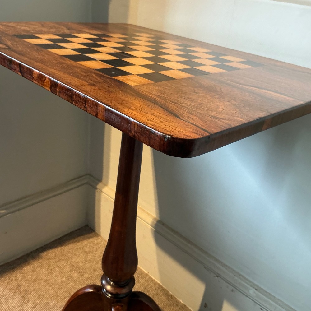 An antique dark wood pedestal chess table featuring an inlaid checkerboard surface top and a turned stem on four splayed legs. View IV