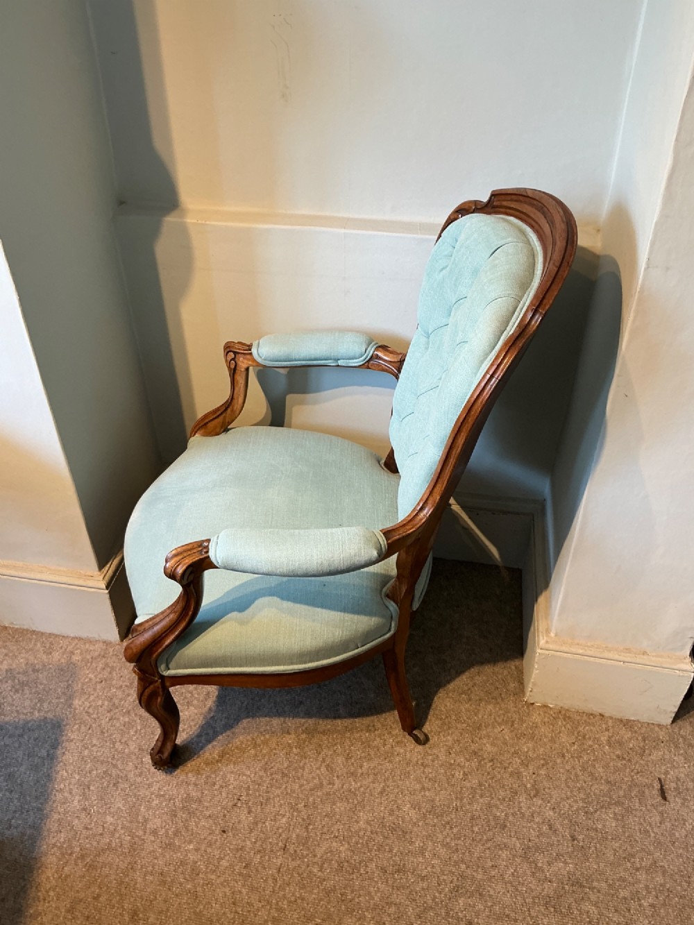 A Victorian carved rosewood open armchair featuring light blue button-tufted upholstery, padded armrests, and cabriole legs on brass castors. View V
