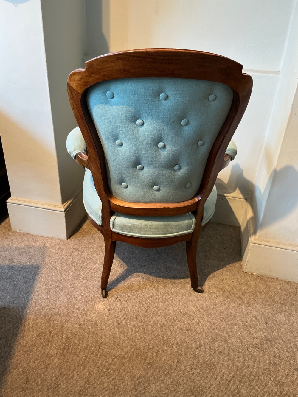 A Victorian carved rosewood open armchair featuring light blue button-tufted upholstery, padded armrests, and cabriole legs on brass castors. View VI