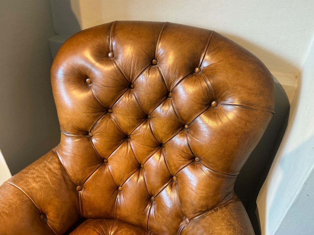 A Victorian warm brown leather armchair featuring deep button tufting, brass stud detailing, and turned wood front legs on castors. View II