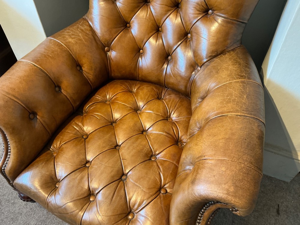 A Victorian warm brown leather armchair featuring deep button tufting, brass stud detailing, and turned wood front legs on castors. View III
