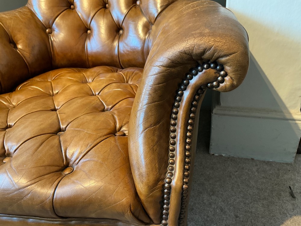 A Victorian warm brown leather armchair featuring deep button tufting, brass stud detailing, and turned wood front legs on castors. View IV