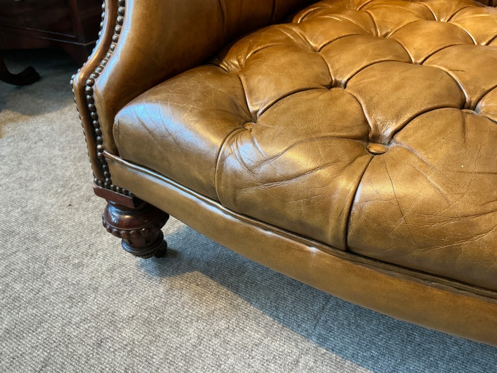 A Victorian warm brown leather armchair featuring deep button tufting, brass stud detailing, and turned wood front legs on castors. View VI