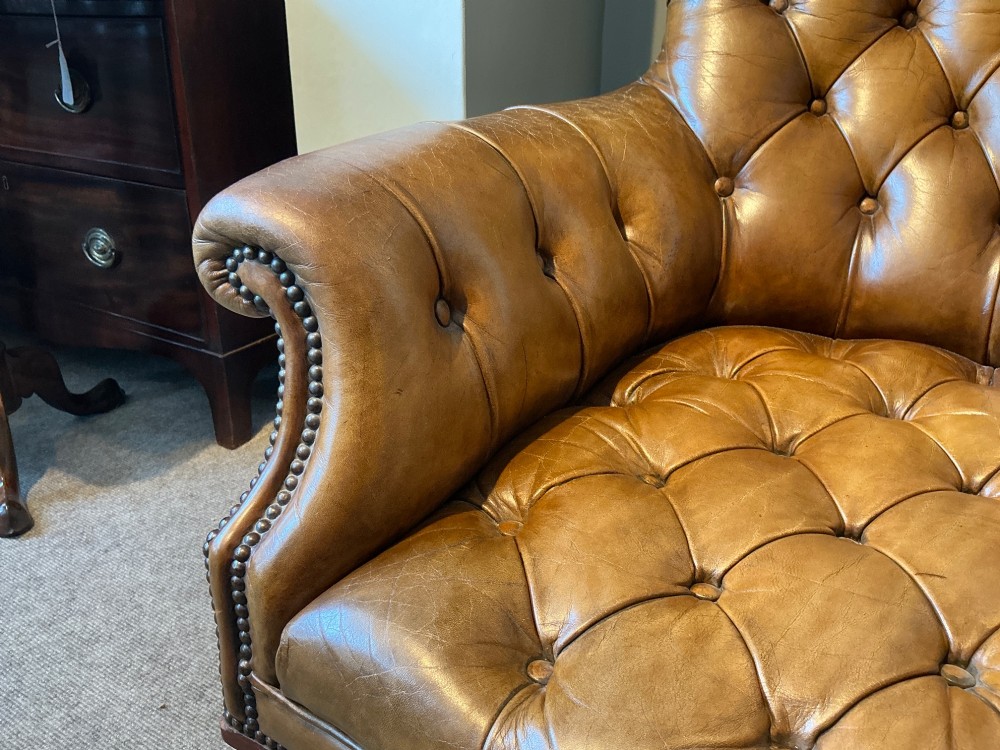 A Victorian warm brown leather armchair featuring deep button tufting, brass stud detailing, and turned wood front legs on castors. View VII