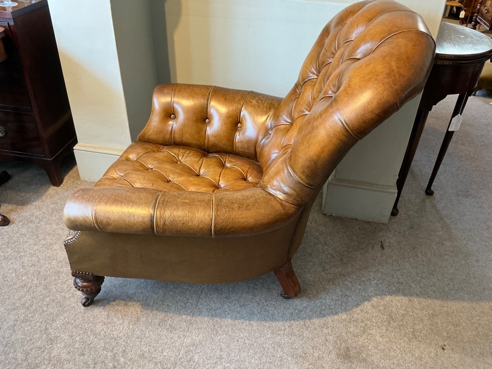 A Victorian warm brown leather armchair featuring deep button tufting, brass stud detailing, and turned wood front legs on castors. View VIII