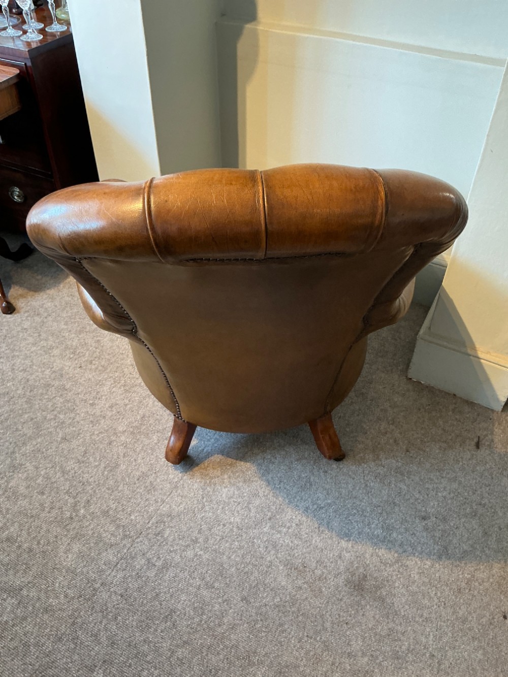 A Victorian warm brown leather armchair featuring deep button tufting, brass stud detailing, and turned wood front legs on castors. View IX