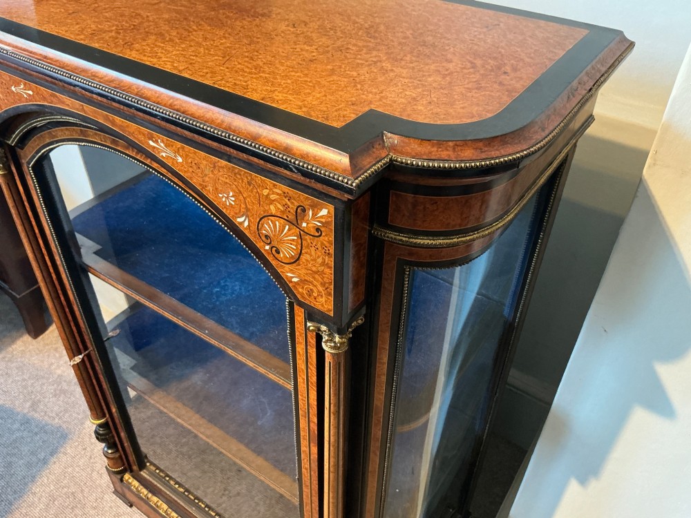 A Victorian burr walnut pier cabinet with ebonised borders, floral marquetry inlays, gilt ormolu mounts, and a single glass door opening to a blue velvet-lined interior. View V