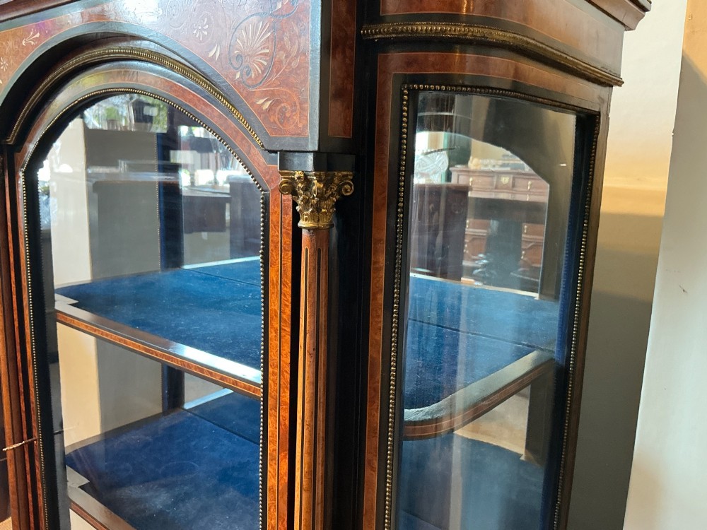 A Victorian burr walnut pier cabinet with ebonised borders, floral marquetry inlays, gilt ormolu mounts, and a single glass door opening to a blue velvet-lined interior. View VI