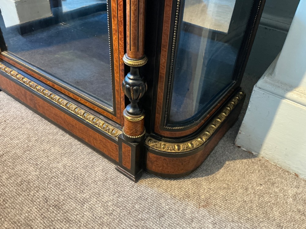 A Victorian burr walnut pier cabinet with ebonised borders, floral marquetry inlays, gilt ormolu mounts, and a single glass door opening to a blue velvet-lined interior. View VII