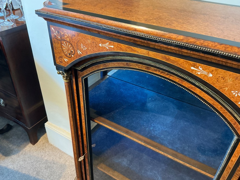 A Victorian burr walnut pier cabinet with ebonised borders, floral marquetry inlays, gilt ormolu mounts, and a single glass door opening to a blue velvet-lined interior. View VIII
