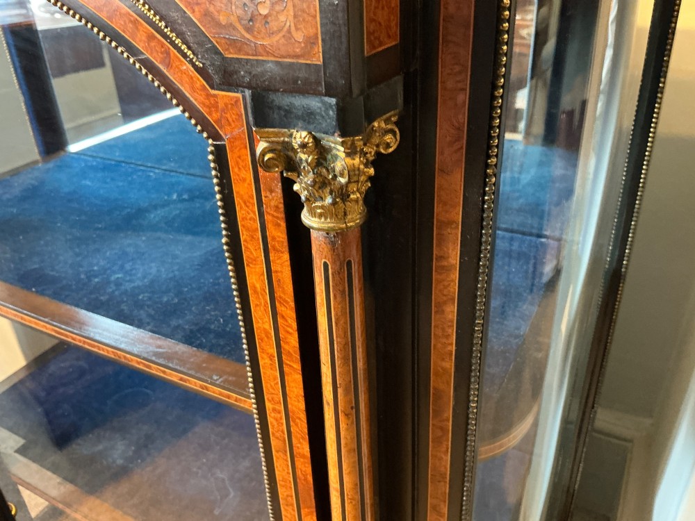 A Victorian burr walnut pier cabinet with ebonised borders, floral marquetry inlays, gilt ormolu mounts, and a single glass door opening to a blue velvet-lined interior. View IX