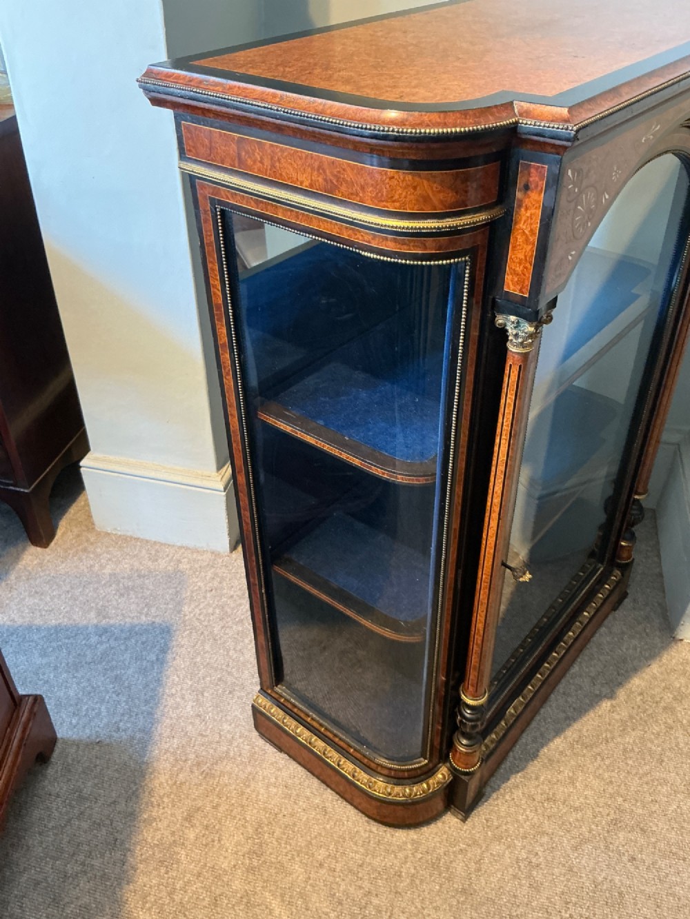 A Victorian burr walnut pier cabinet with ebonised borders, floral marquetry inlays, gilt ormolu mounts, and a single glass door opening to a blue velvet-lined interior. View X