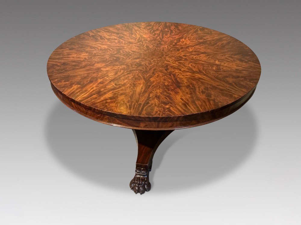 A circular antique mahogany centre table featuring a radially segmented flame veneer top supported by a central pedestal with carved claw feet. View II