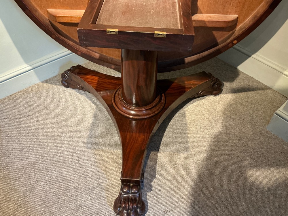A circular antique mahogany centre table featuring a radially segmented flame veneer top supported by a central pedestal with carved claw feet. View VII