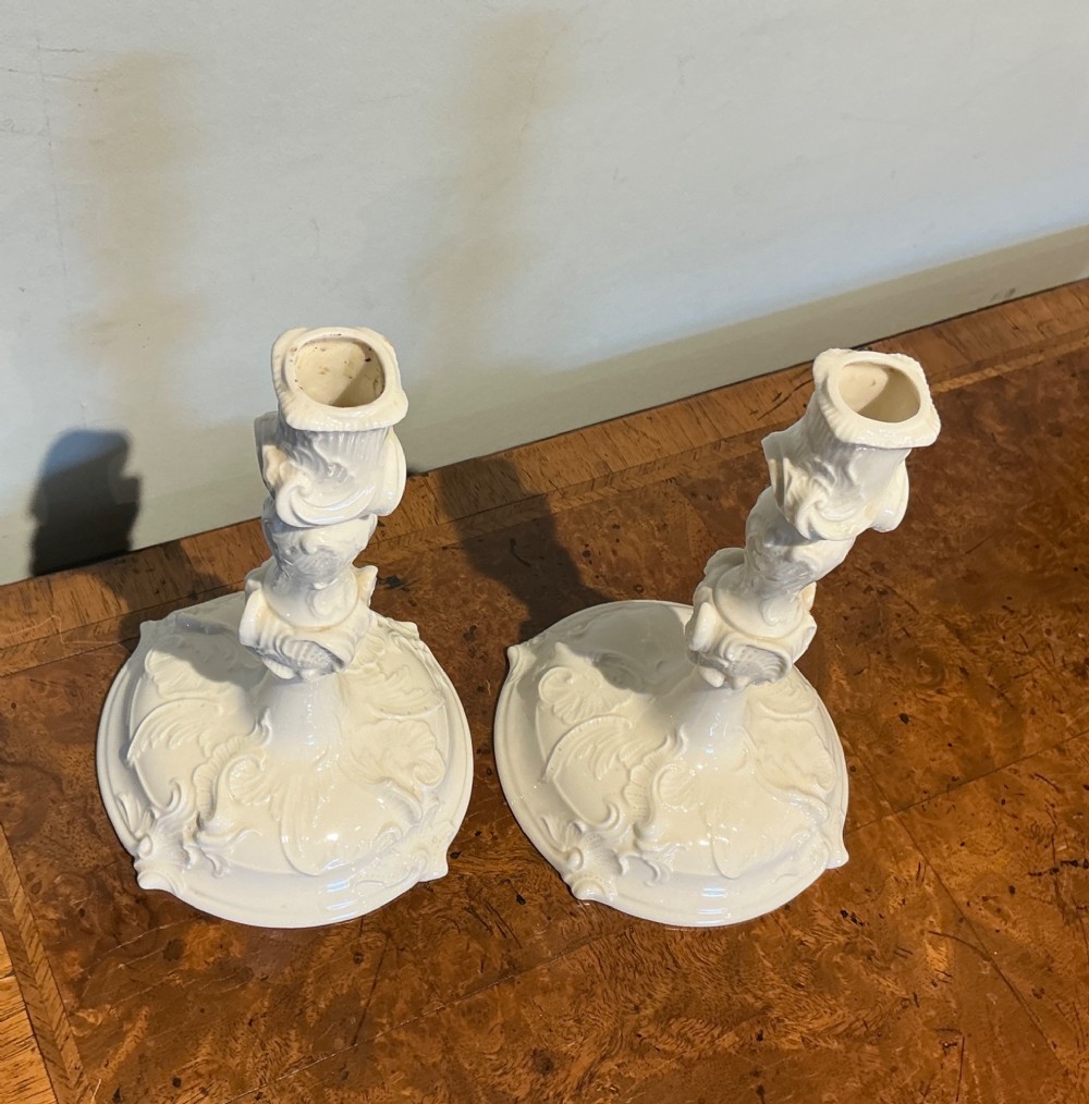 A pair of off-white glazed porcelain candlesticks featuring sculpted Rococo scrollwork and shell motifs on wide circular bases. View II