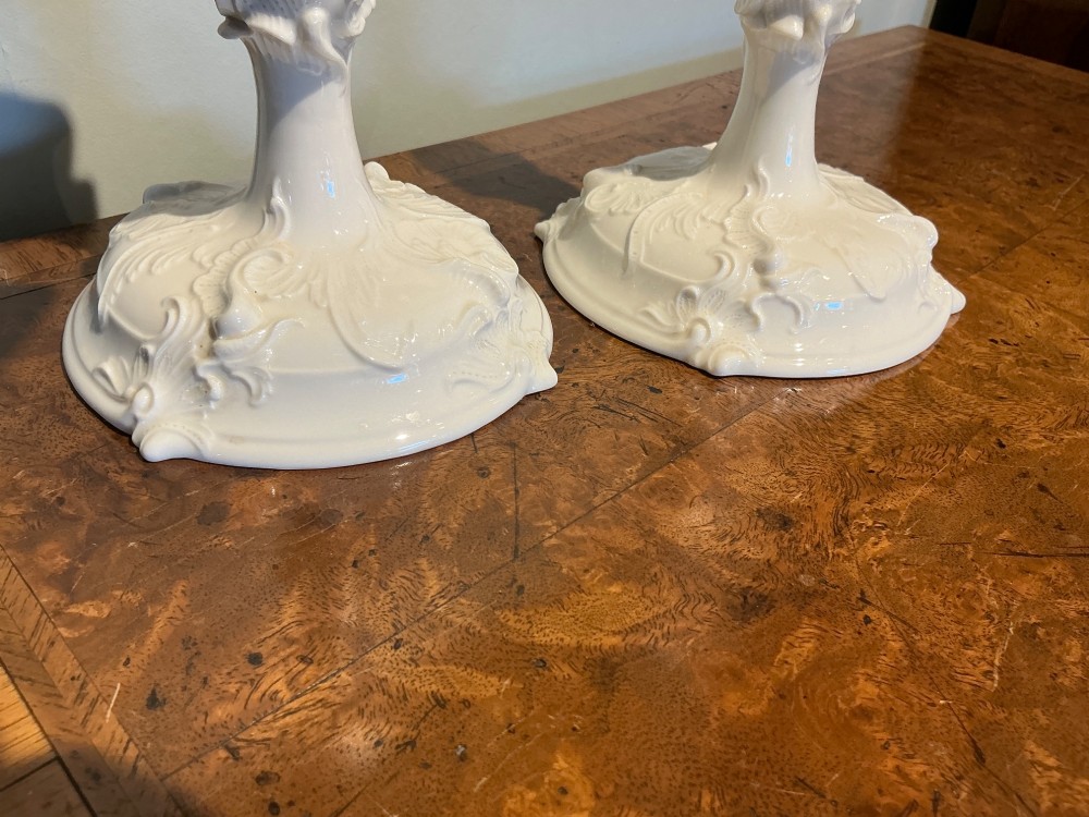 A pair of off-white glazed porcelain candlesticks featuring sculpted Rococo scrollwork and shell motifs on wide circular bases. View III
