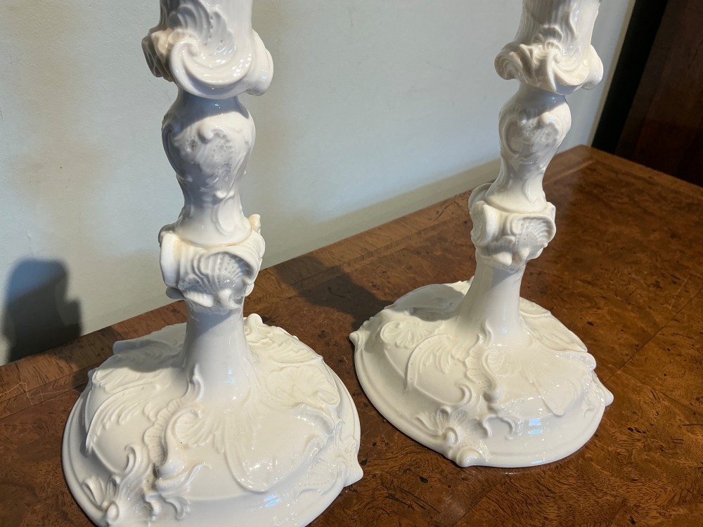 A pair of off-white glazed porcelain candlesticks featuring sculpted Rococo scrollwork and shell motifs on wide circular bases. View IV