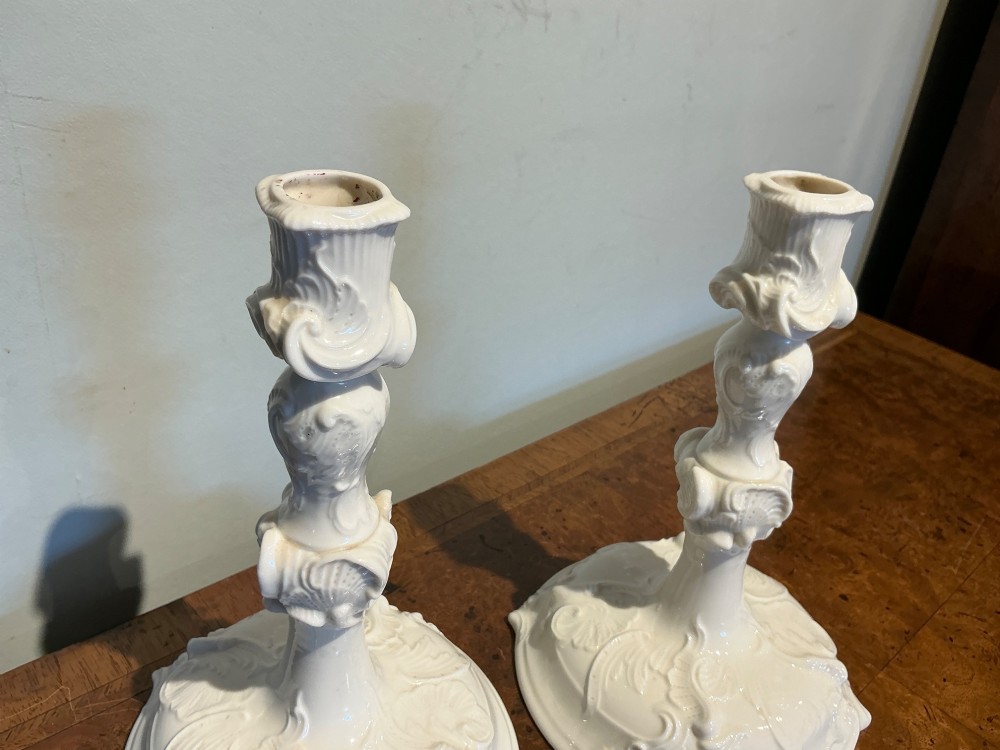 A pair of off-white glazed porcelain candlesticks featuring sculpted Rococo scrollwork and shell motifs on wide circular bases. View V