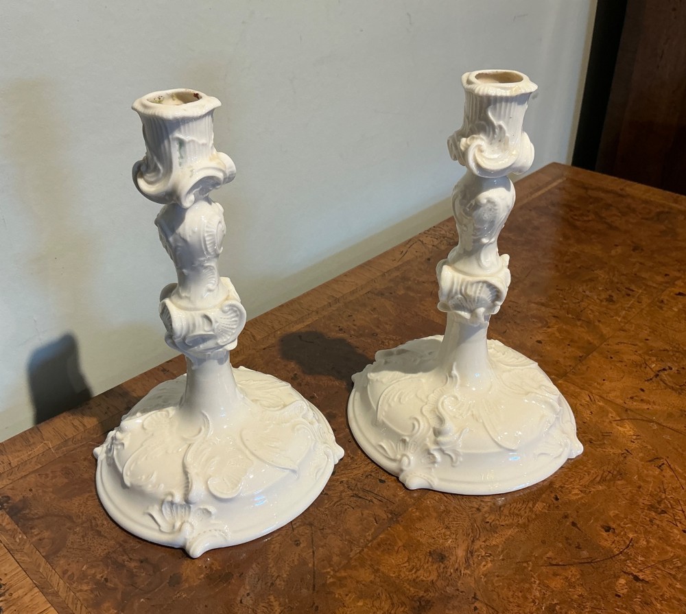 A pair of off-white glazed porcelain candlesticks featuring sculpted Rococo scrollwork and shell motifs on wide circular bases. View VI