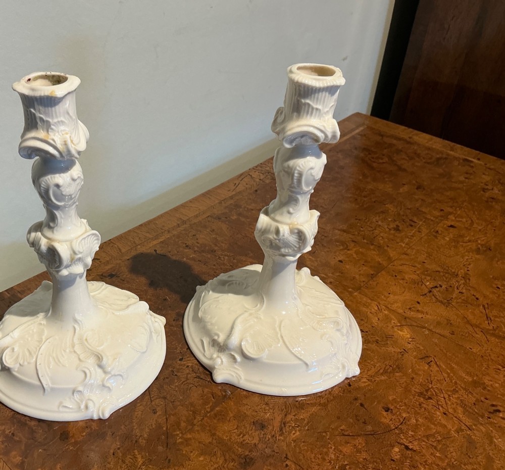 A pair of off-white glazed porcelain candlesticks featuring sculpted Rococo scrollwork and shell motifs on wide circular bases. View VII