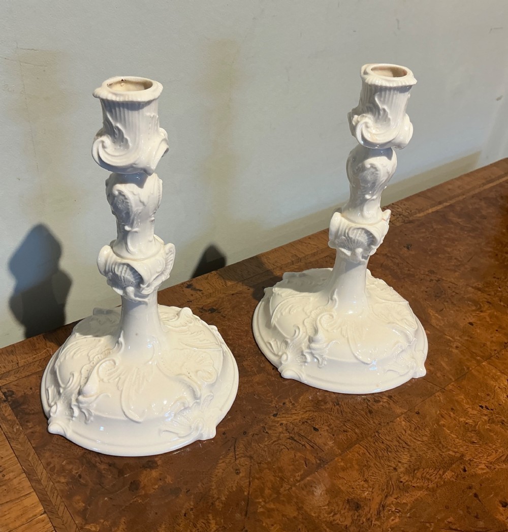A pair of white glazed porcelain candlesticks featuring ornate Rococo relief moulding and scrollwork bases.