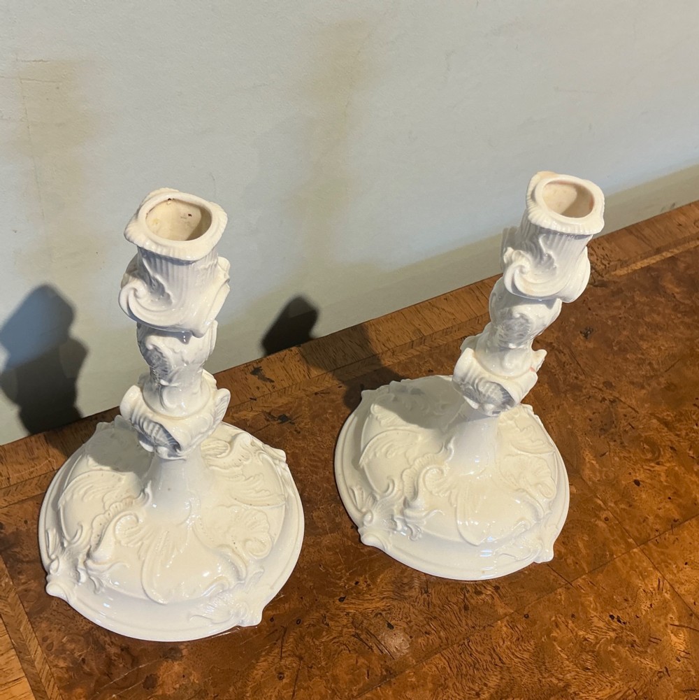 A pair of white glazed porcelain candlesticks featuring ornate Rococo relief moulding and scrollwork bases. View II